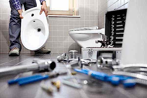 Expert Bathroom Leak Repairs Close-up of a plumber fixing a leak in a bathroom, focusing on a toilet, pipes, various plumbing equipment, and tools, provided by AD Plumbing, Heating, and Electrical.