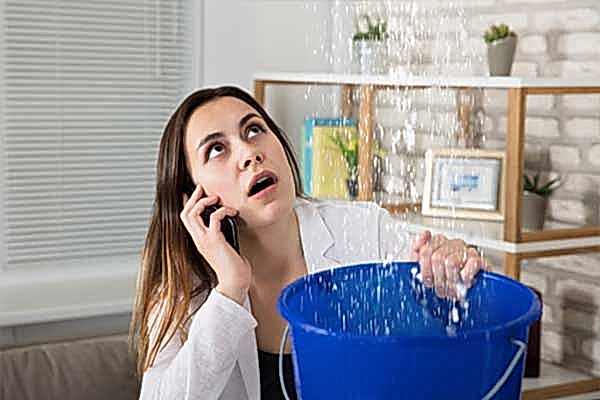 Ceiling Leak Emergency in Manchester Woman in distress with a bucket, capturing water from a ceiling leak, while on the phone in an emergency situation.