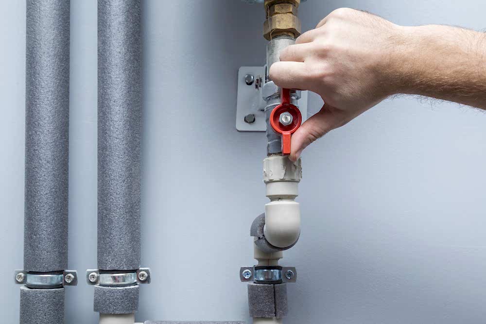 Close-up of a technician's hands working on a Boiler pipe mechanism, resembling a stop valve, during a boiler leak repair by AD Plumbing, Heating, and Electrical."