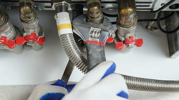 Close-up of a technician's hands using an adjustable spanner on a valve during a boiler leak repair by AD Plumbing, Heating, and Electrical.
