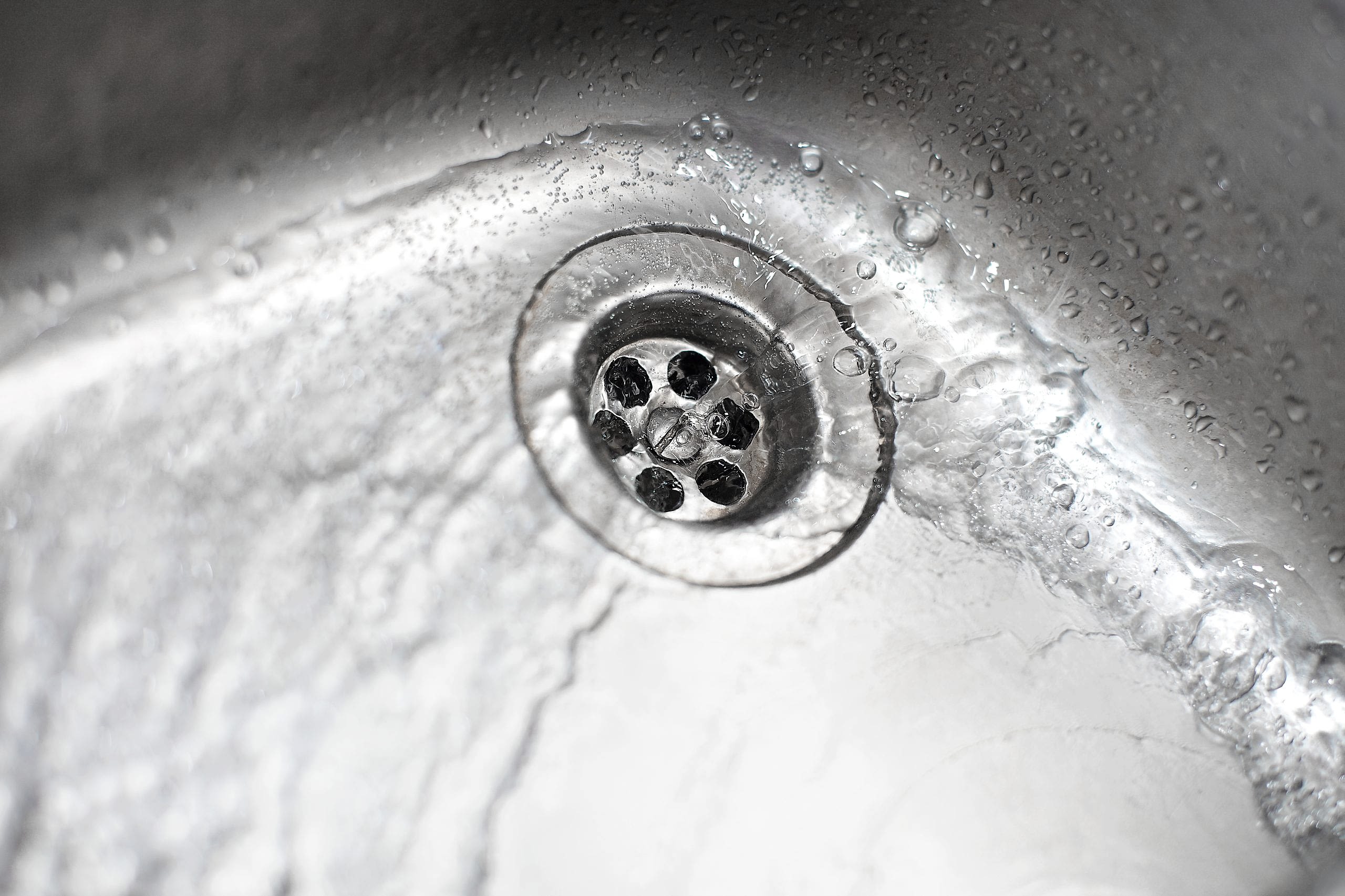 Close-up of a modern kitchen sink plug hole with clean water, showcasing a successful drain unblocking by AD Plumbing, Heating, and Electrical.